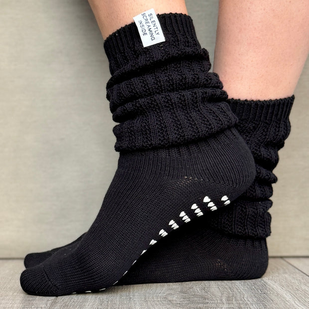A pair of black slouch socks with grip pads on the sole, featuring a cozy, casual style.